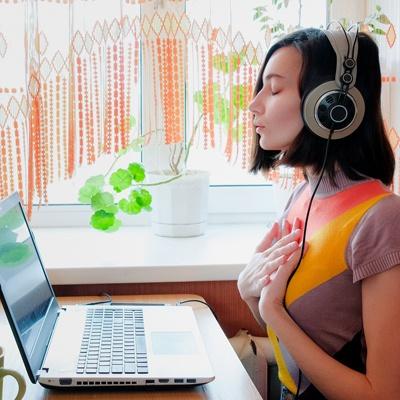 a young woman with headphones on doing a guided meditation on her computer