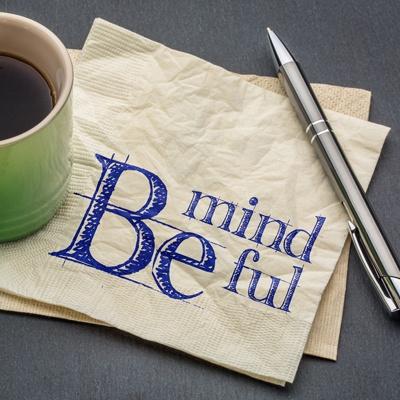 a napkin that says Be Mindful, next to a coffee cup and pen
